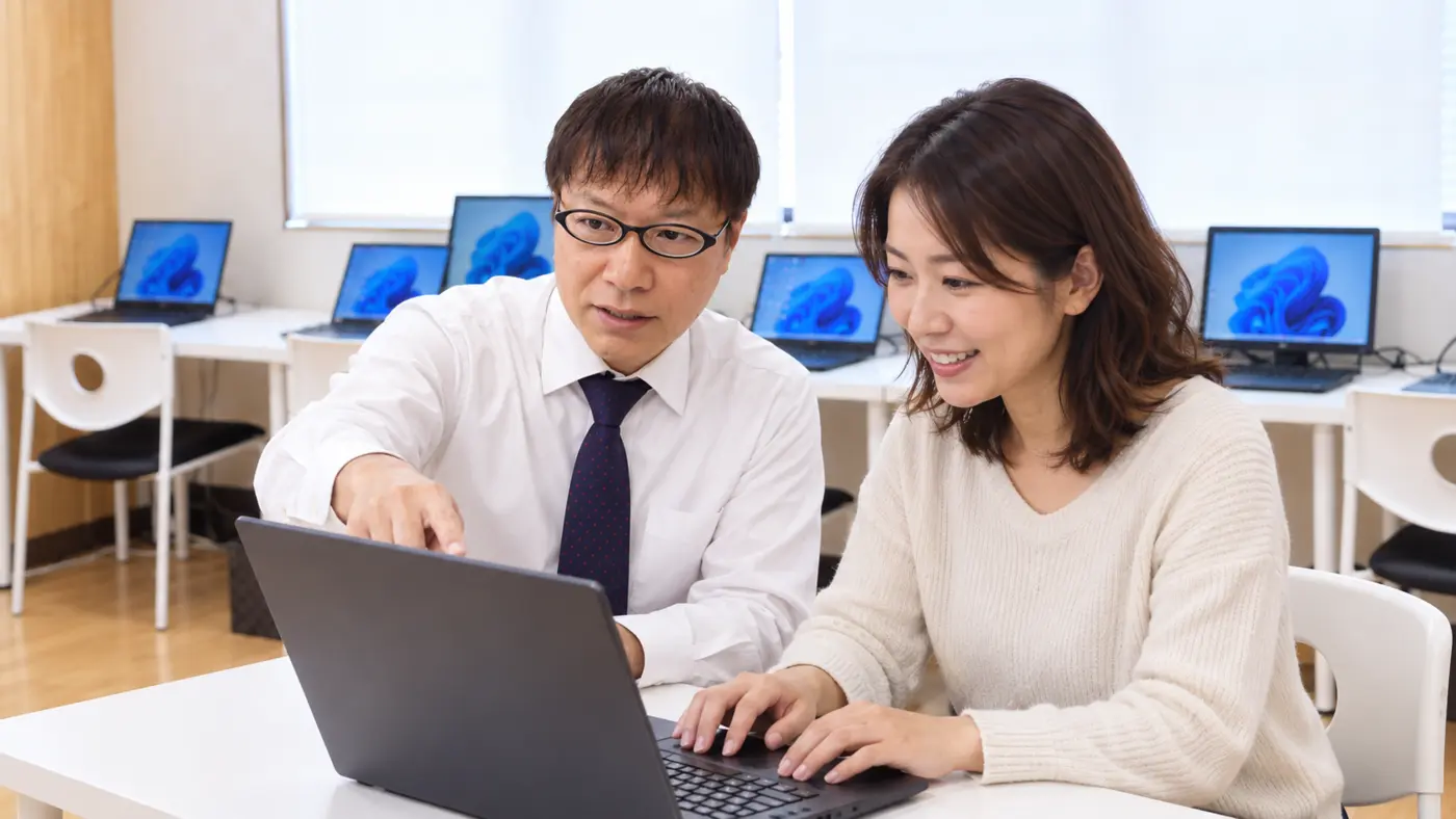 女性講師が初心者の受講生にパソコン操作を教える様子